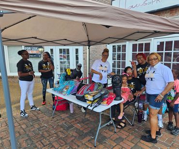 Community event with people under a canopy distributing backpacks.