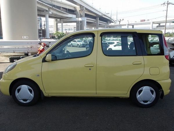 Yellow compact car parked under a highway overpass.