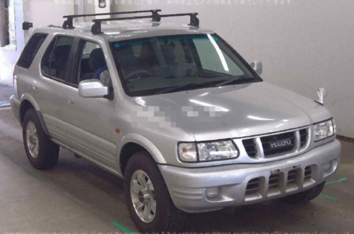 Silver Isuzu SUV parked indoors with roof rack and side mirrors.
