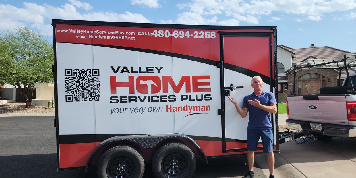 Man stands next to a handyman service trailer with contact details.