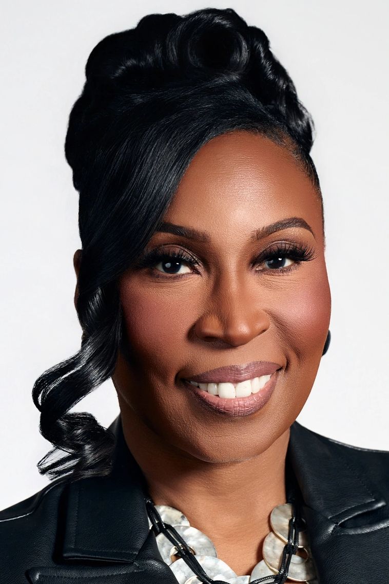 Black woman headshot, smiling wearing hair up and one curl hanging, silver necklace and black jacket