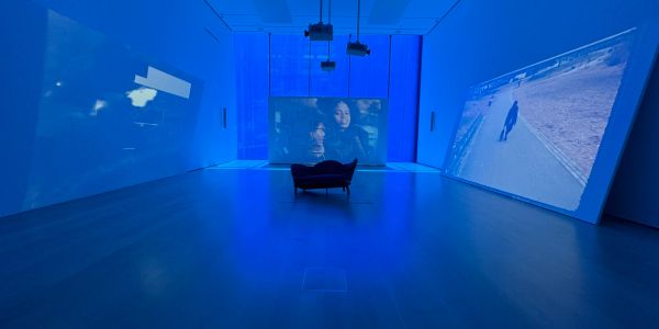 A dark room with blue lighting and three large projection screens showing different scenes.