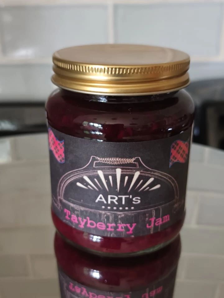 A jar of ART's Tayberry Jam with a gold lid and dark label.