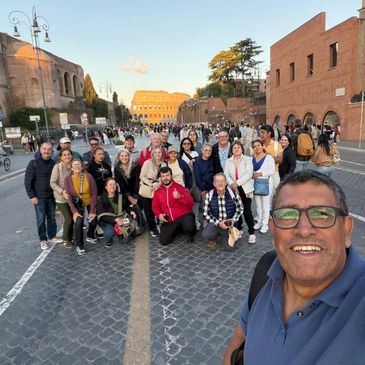 A large group taking a selfie near the Colosseum in Rome during sunset.
