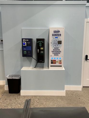 Laundry soap and vending machines against a pale blue wall in a laundry room.