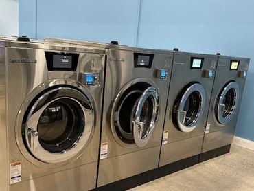 Four modern stainless steel front-load washing machines in a clean laundry room.