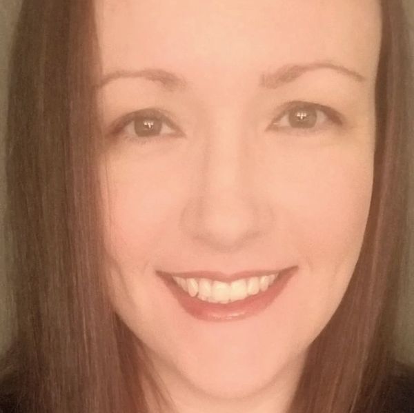 A smiling woman with long brown hair. She is wearing a heart-shaped necklace that says Mom.
