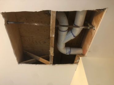 Ceiling hole showing pipes and wooden framing.
