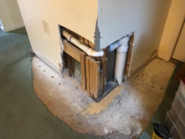 Exposed plumbing inside a damaged wall corner.