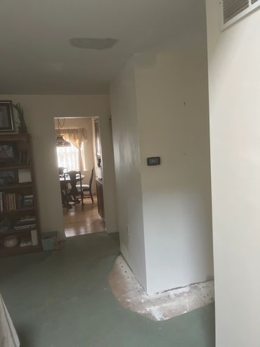 Room with damaged ceiling, thermostat, and partially removed carpet.