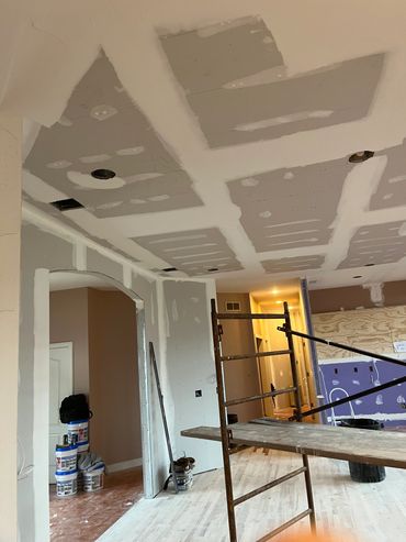 Room under renovation with drywall installation and scaffolding.