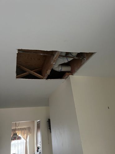 Ceiling hole revealing pipes and wooden beams.