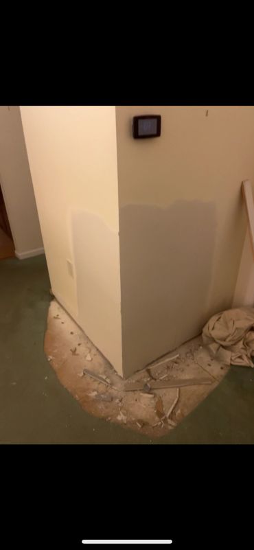 Wall corner with damaged carpet and debris.