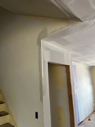 Interior wall with unfinished drywall and paint patches near staircase.