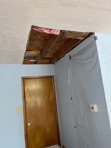 Ceiling with a removed panel exposing insulation and wooden beams.