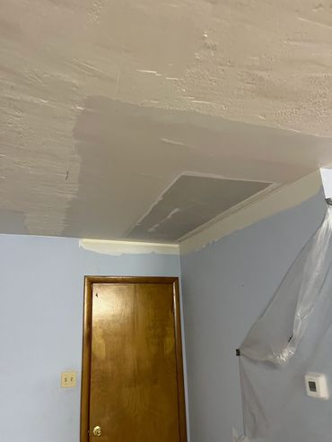 Ceiling under renovation with a wooden door and plastic sheet on the wall.