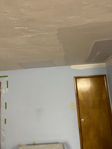 Ceiling with plaster patches and a wooden door in a room.