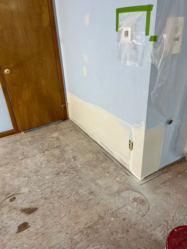 Room renovation with patched wall and bare plywood floor.