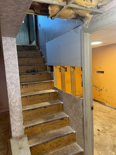 Basement stairs under renovation with exposed insulation and bare walls.