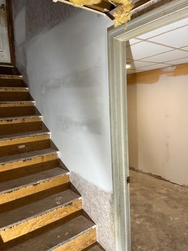 Wooden stairs with partially painted wall and exposed ceiling insulation.