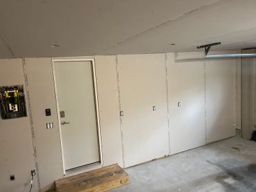 Unfinished interior wall with drywall and electrical panel.