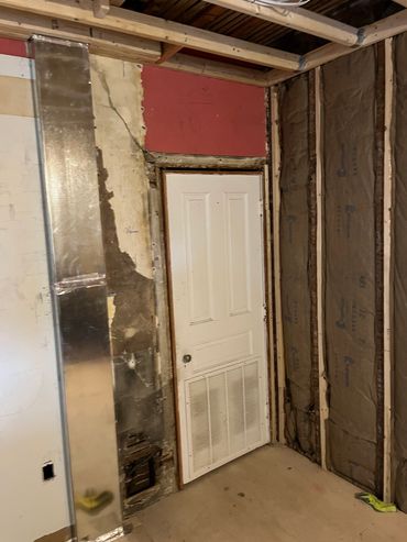 Under construction room with exposed insulation and a white door.