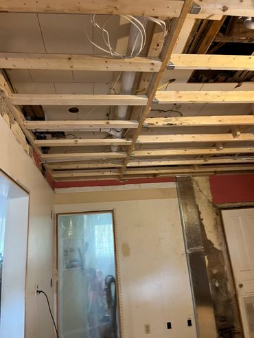 Room under renovation with exposed ceiling beams and pipes.