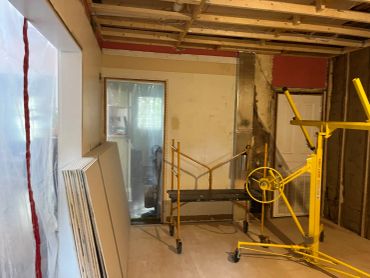 Room under renovation with construction equipment and drywall sheets.