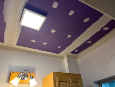 Ceiling with purple drywall and patchwork near a light fixture.
