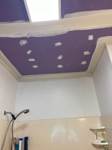 Ceiling with purple paint and patches in a bathroom.