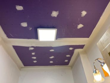 Ceiling with purple paint and patched spots around a light fixture.