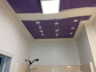 Ceiling with purple drywall and shower head in bathroom.