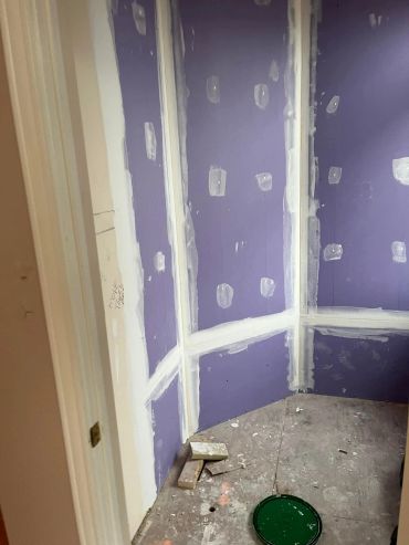 Room under renovation with purple drywall and patching.