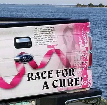 Back of a pick-up truck with a "race for a cure!" text on the breast cancer awareness-themed wrap