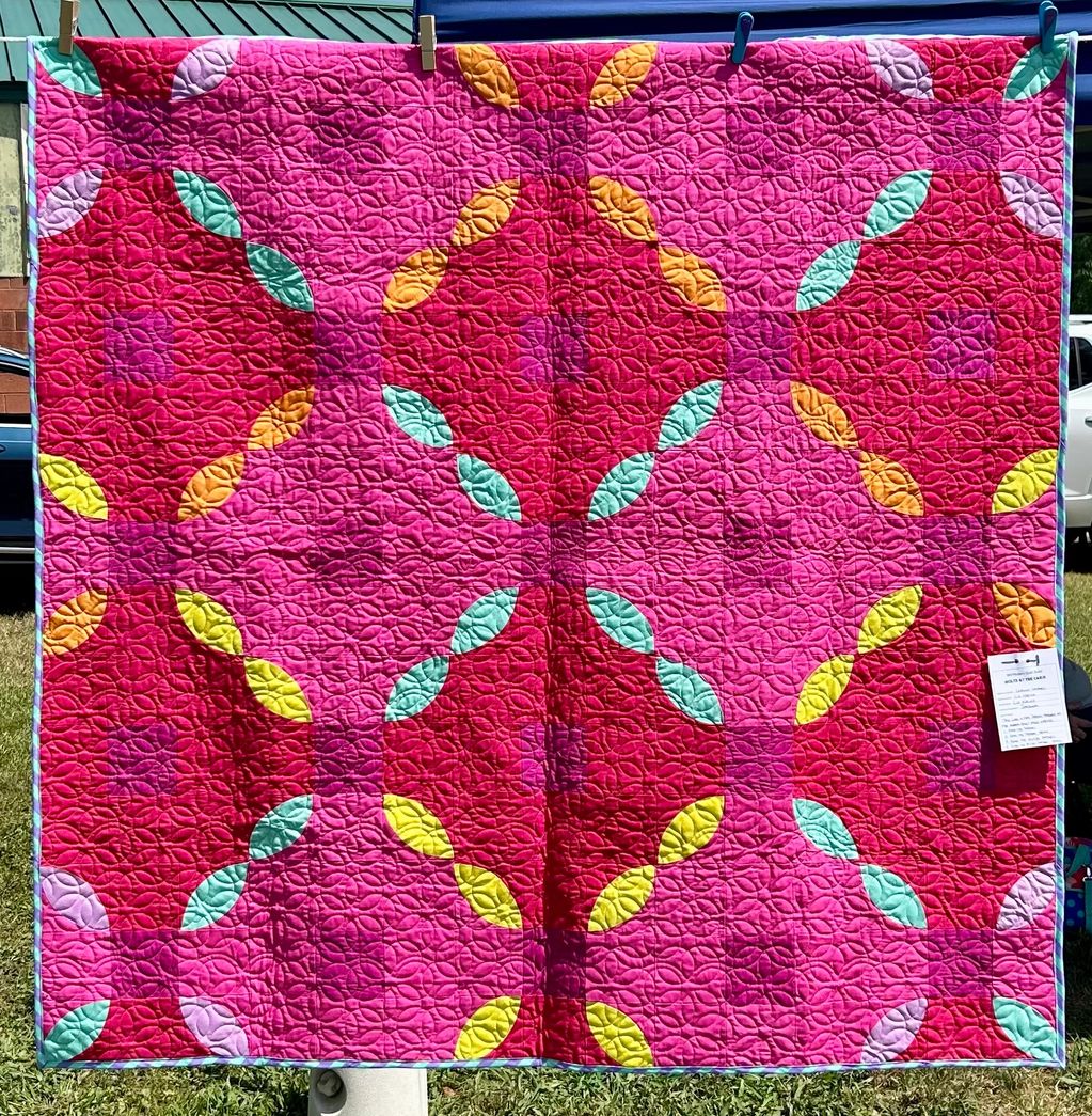 Bright pink quilt with colorful leaf-shaped patterns and intricate stitching.