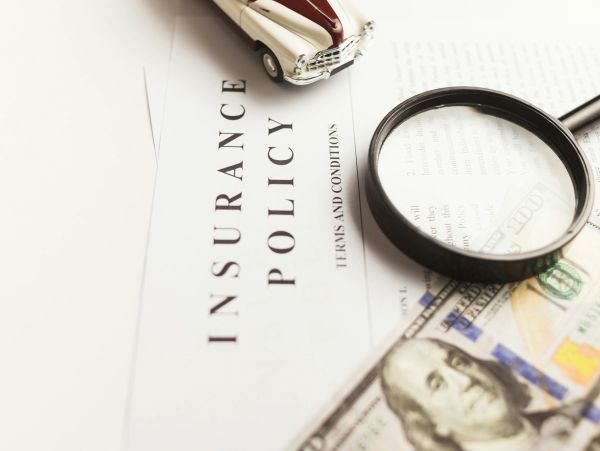 Magnifying glass on car insurance papers and money.