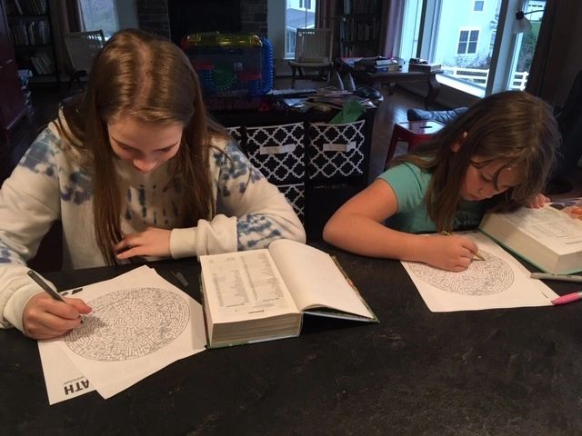 Two girls solving word search puzzles at a table with dictionaries.