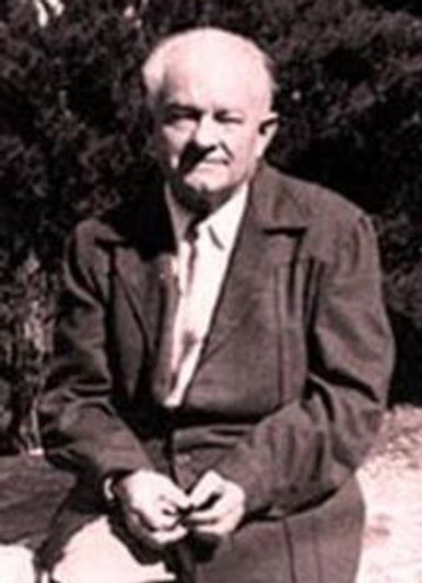 Ernest Holmes sitting outdoors, dressed formally in a coat and tie.