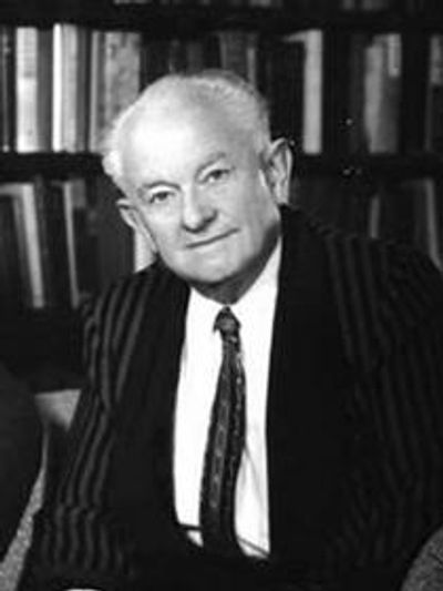 Black and white portrait of Science of Mind founder Ernest Holmes in a striped suit sitting indoors.