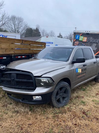 Damaged pickup truck parked on grass near work trucks on a cloudy day.