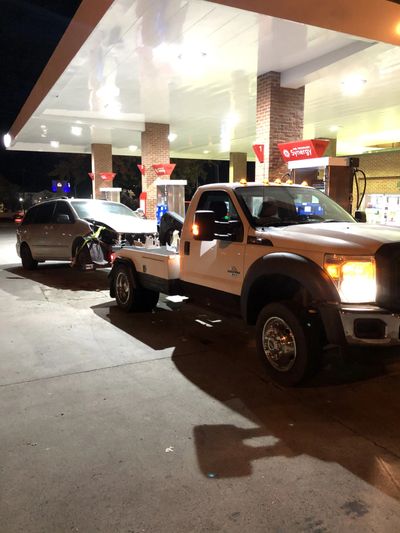 Tow truck at gas station towing a silver car at night.