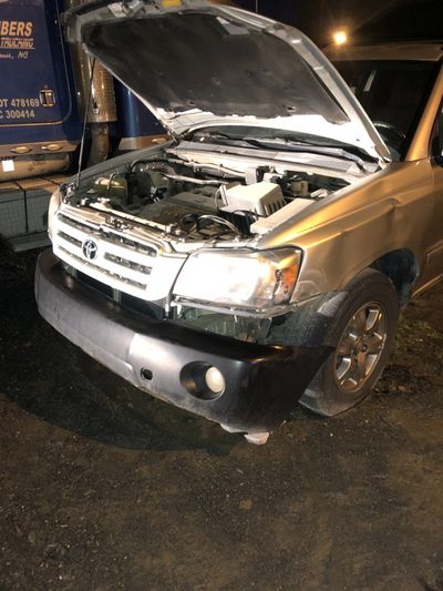 A gold SUV with its hood open, parked on a dirt surface at night.