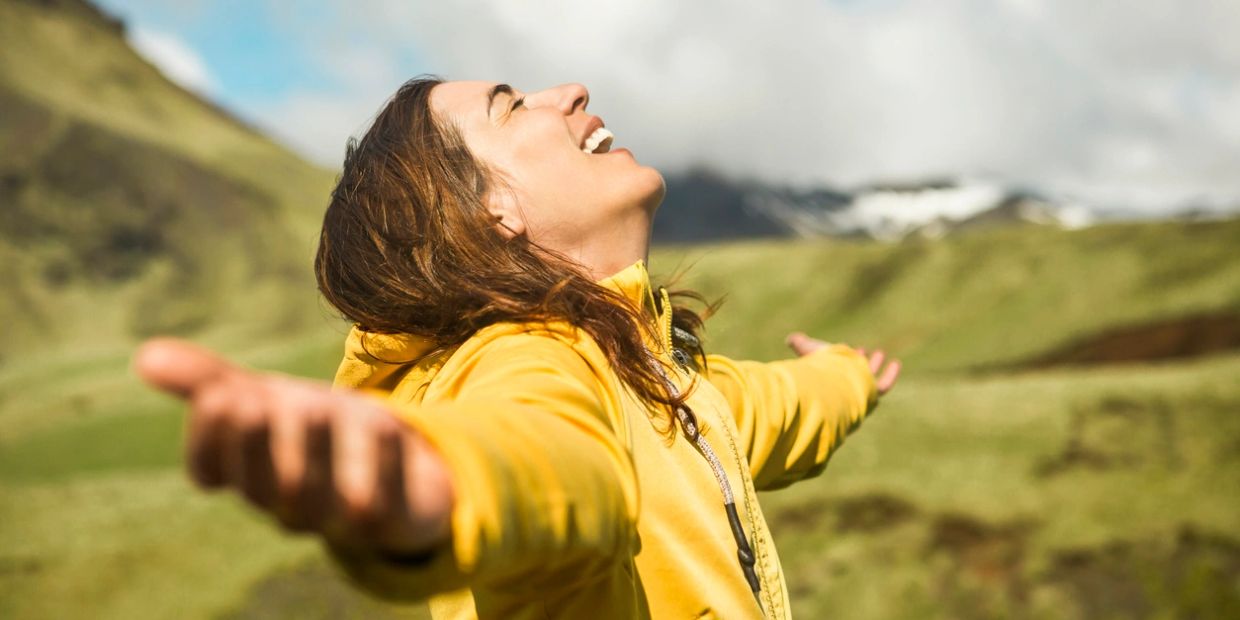 Woman in yellow jacket enjoying nature with arms wide open.