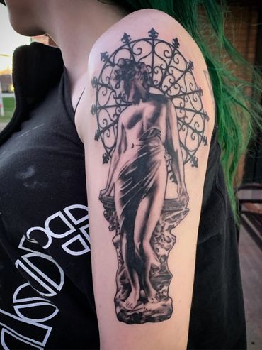 black and gray realism female statue tattoo with black ironwork in the background