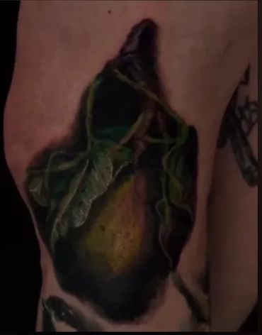 color realism tattoo of a pear on a leg in dramatic lighting