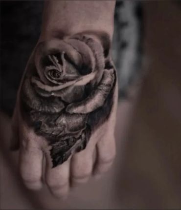 black and gray realism hand tattoo of a rose on a hand