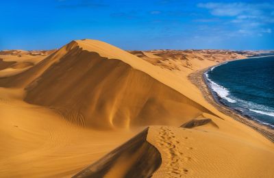 Sand dunes meet the ocean under a clear sky.