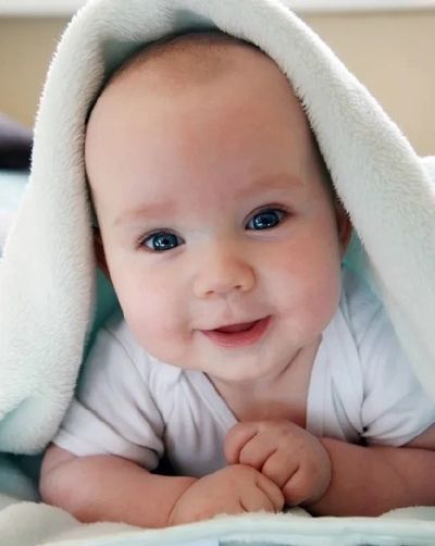Smiling baby with blue eyes under a blanket.