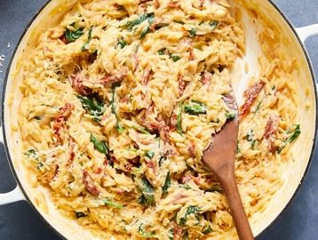 Creamy pasta with spinach and sun-dried tomatoes in a white pot.