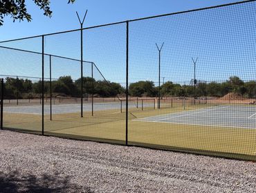 Empty tennis courts surrounded by a chain-link fence on a sunny day.